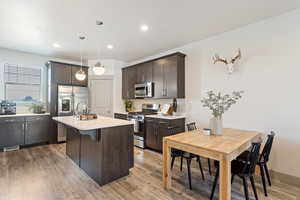Kitchen with appliances with stainless steel finishes, light countertops, dark brown cabinets, a center island with sink, and light wood-style flooring