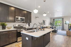 Kitchen featuring appliances with stainless steel finishes, a sink, open floor plan, light countertops, and dark brown cabinets