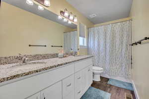 Bathroom with double vanity, toilet, and wood finished floors