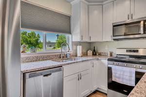 Kitchen featuring appliances with stainless steel finishes, a sink, white cabinetry, and light stone counters