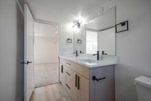 Full bath featuring double vanity, a textured ceiling, toilet, wood finished floors, and baseboards