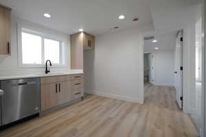 Kitchen with a sink, stainless steel dishwasher, light brown cabinets, light wood-style floors, and light countertops