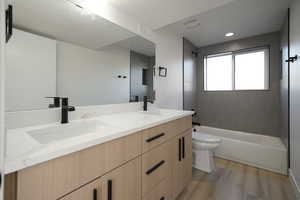 Bathroom featuring wood finished floors, toilet, double vanity,  shower combination, and a textured ceiling