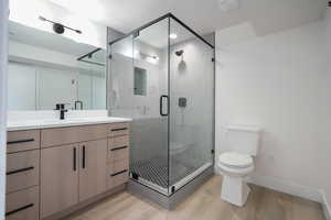 Bathroom featuring toilet, vanity, wood finished floors, a shower stall, and baseboards