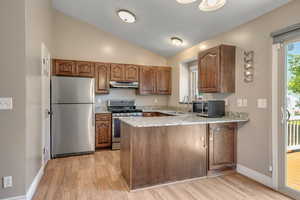 Kitchen featuring stainless steel appliances, under cabinet range hood, a peninsula, a sink, and light wood finished floors