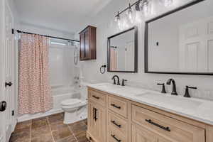 Full bathroom featuring double vanity, shower / bath combo with shower curtain, toilet, and stone finish flooring