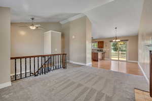 Unfurnished room with light colored carpet, lofted ceiling, a chandelier, ceiling fan, and baseboards