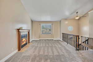 Unfurnished living room featuring carpet flooring, a tile fireplace, ceiling fan, baseboards, and lofted ceiling