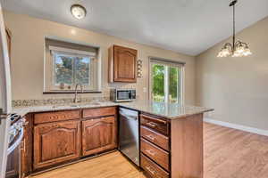 Kitchen with stainless steel appliances, a sink, a peninsula, light wood-type flooring, and a textured ceiling
