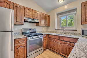 Kitchen featuring appliances with stainless steel finishes, under cabinet range hood, a sink, lofted ceiling, and light wood finished floors