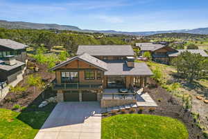 Contemporary home featuring a garage, driveway, stone siding, a mountain view, and a front yard