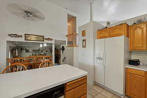 Kitchen featuring white refrigerator with ice dispenser, dishwasher, light countertops, ceiling fan, and brown cabinets