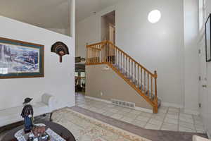 Entrance foyer with tile patterned floors, stairway, a high ceiling, and baseboards