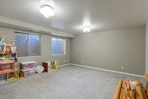 Recreation room featuring carpet floors, a textured ceiling, and baseboards