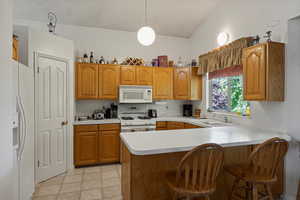 Kitchen with white appliances, a sink, a peninsula, light countertops, and lofted ceiling