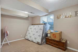 Bedroom with a textured ceiling, light carpet, and baseboards