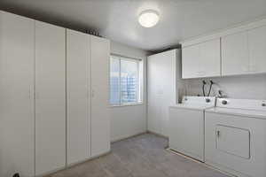 Washroom featuring washing machine and dryer, cabinet space, light carpet, and a textured ceiling