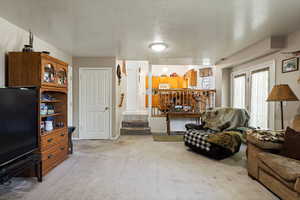 Living area featuring a textured ceiling, light colored carpet, and stairs