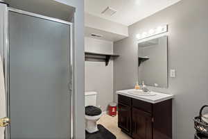 Full bath featuring toilet, vanity, a stall shower, a textured ceiling, and tile patterned floors