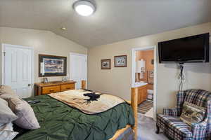 Bedroom featuring light carpet, lofted ceiling, ensuite bathroom, and a textured ceiling