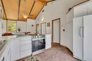 Kitchen featuring freestanding refrigerator, stainless steel electric stove, wooden ceiling with exposed beams, high vaulted ceiling, and a ceiling fan