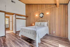 Bedroom with wood walls, wooden ceiling, wood finished floors, a closet, and high vaulted ceiling