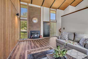 Living room featuring high vaulted ceiling, wooden ceiling with exposed beams, healthy amount of natural light, wood finished floors, and wooden walls