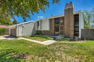 Mid-century modern home with a chimney, brick siding, entry steps, an attached garage, and driveway