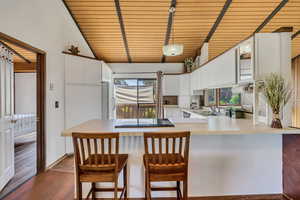 Kitchen featuring a peninsula, freestanding refrigerator, black electric cooktop, dark wood finished floors, and white cabinets