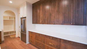 Kitchen featuring high end fridge, light wood-style floors, arched walkways, light countertops, and white cabinets