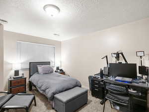 Bedroom with light carpet, a textured ceiling, a desk, and baseboards