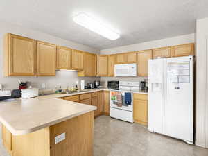 Kitchen featuring white appliances, a peninsula, a sink, light countertops, and a textured ceiling