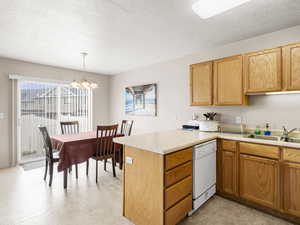 Kitchen with white dishwasher, a sink, a peninsula, light countertops, and a chandelier