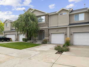 Townhome / multi-family property with an attached garage, stucco siding, driveway, and stone siding
