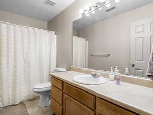 Full bath with toilet, vanity, a textured ceiling, tile patterned flooring, and a shower with shower curtain