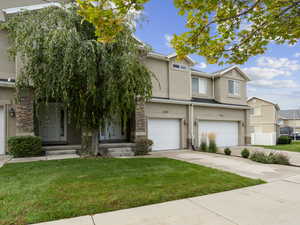 Townhome / multi-family property with stone siding, an attached garage, stucco siding, driveway, and a front lawn