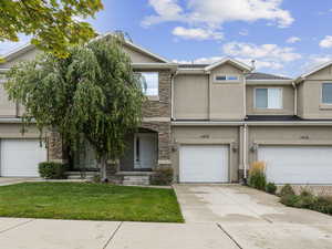 Townhome / multi-family property with stone siding, stucco siding, a front lawn, and an attached garage