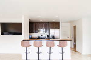 Kitchen featuring appliances with stainless steel finishes, a kitchen breakfast bar, dark brown cabinetry, and baseboards