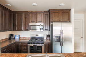 Kitchen featuring stainless steel appliances, dark brown cabinets, and dark countertops