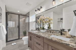 Bathroom with double vanity, toilet, a stall shower, and recessed lighting