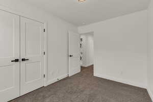 Unfurnished bedroom with stacked washing machine and dryer, carpet flooring, and baseboards