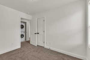 Empty room featuring estacked washer and dryer, carpet floors, and baseboards