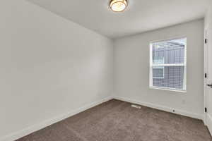 Spare room featuring dark colored carpet, baseboards, and a textured ceiling