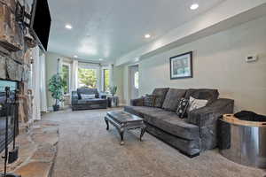 Carpeted living room with recessed lighting, a stone fireplace, and baseboards