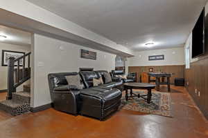 Living area with concrete flooring, stairs, wainscoting, and wood walls