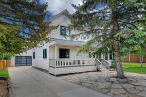 View of front of home featuring a porch, driveway, an outdoor structure, and roof with shingles