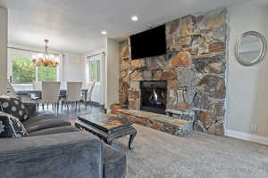 Carpeted living area featuring baseboards, a chandelier, and a stone fireplace
