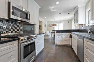 Kitchen with stainless steel appliances, dark countertops, backsplash, a peninsula, and a sink