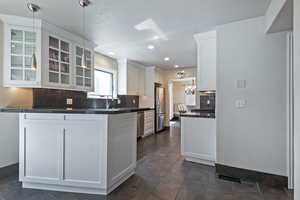 Kitchen with appliances with stainless steel finishes, dark countertops, glass insert cabinets, decorative backsplash, and white cabinets