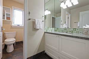 Bathroom with tasteful backsplash, vanity, toilet, and baseboards
